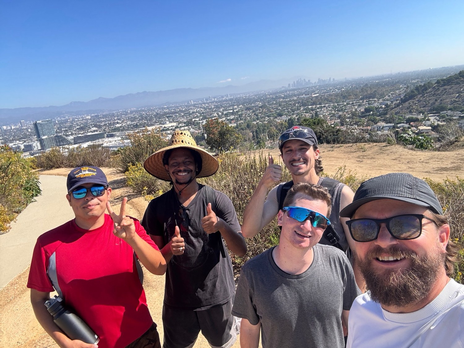 Five people posing on a hillside with a city view behind them