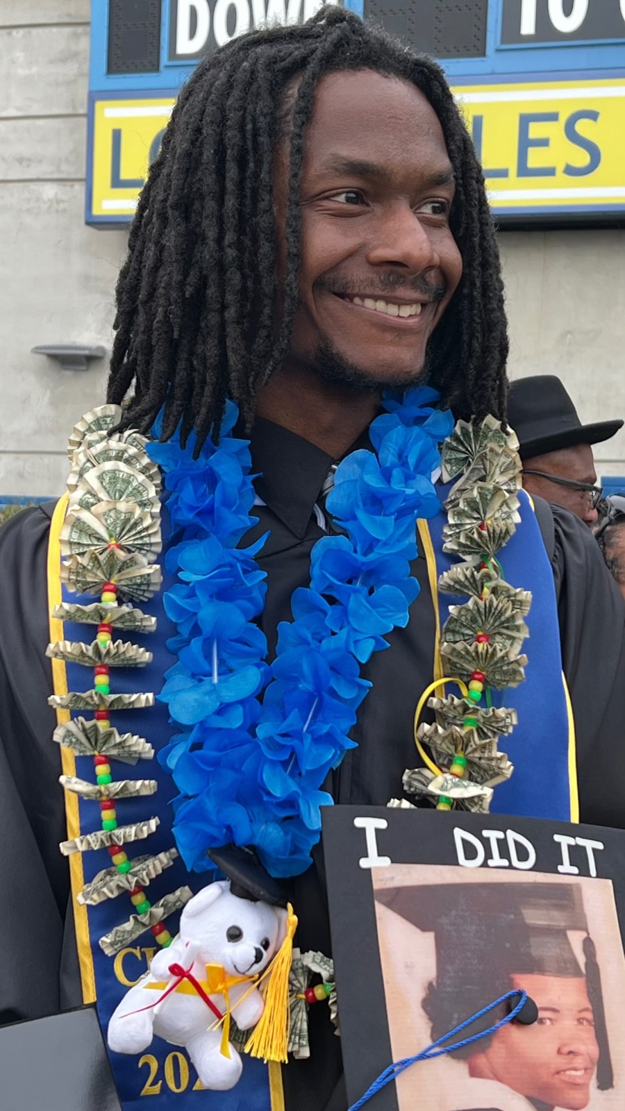 A person wearing leis and holding an “I did it” sign.