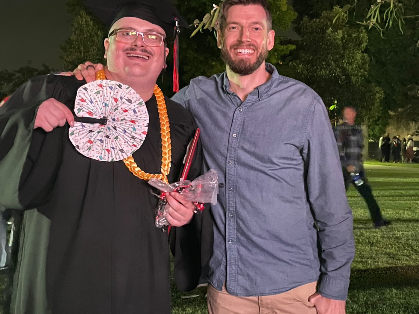 Two people standing together at a graduation celebration, one wearing graduation leis.