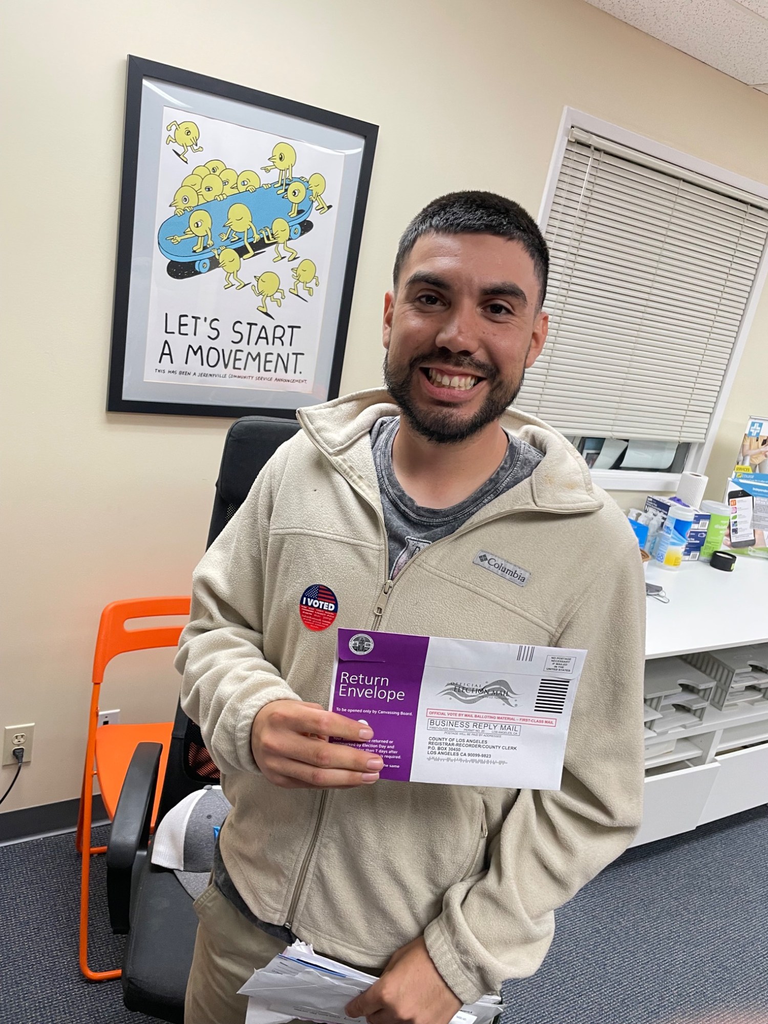A person holding a ballot return envelope and wearing an I Voted sticker.